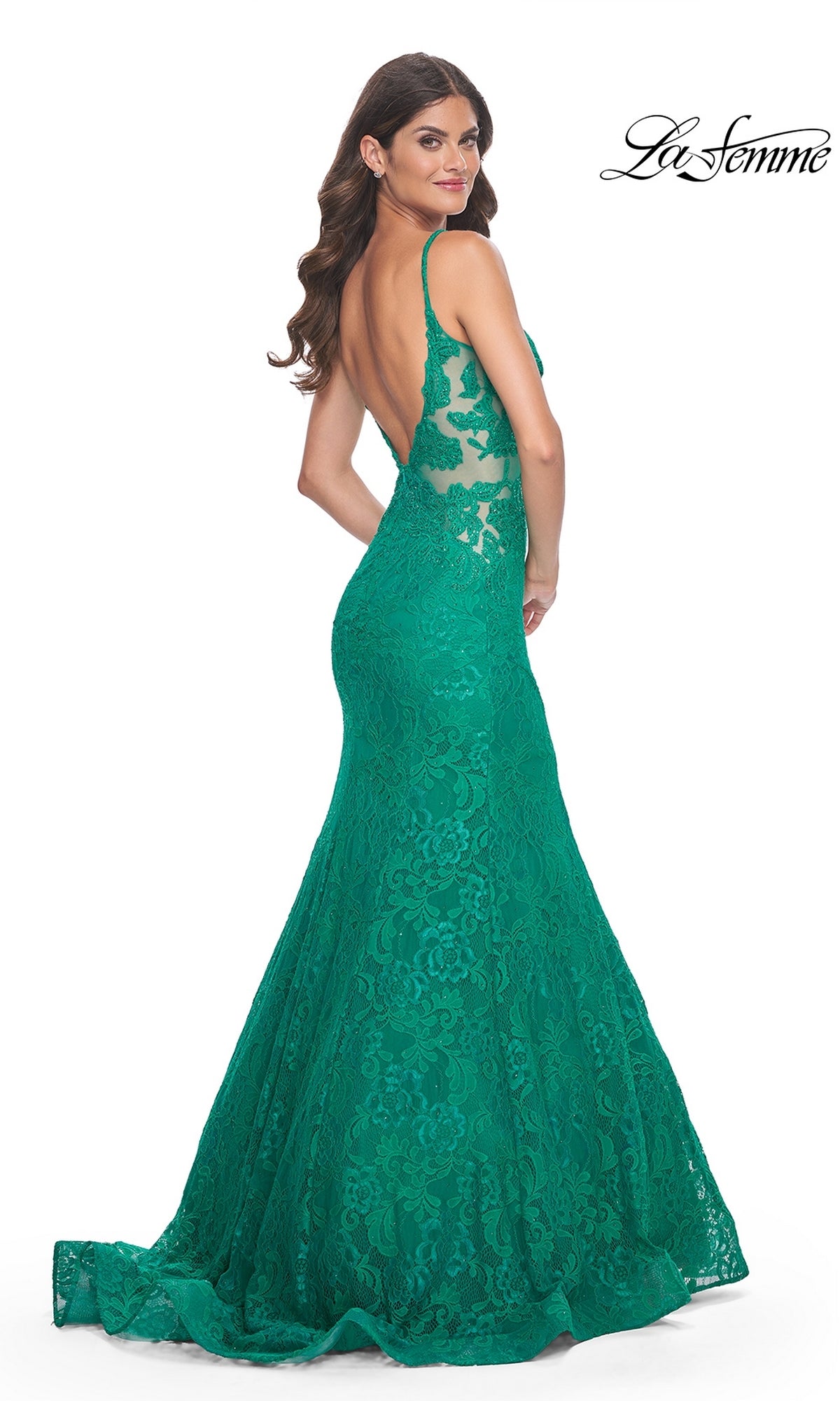 A woman wears the La Femme Sheer-Sides Long Lace Prom Dress 32315, a floor-length green lace gown with thin straps and an open back, standing and looking over her shoulder.